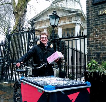 A smiling man stands next to a large cargo bike and holds a box in his hand