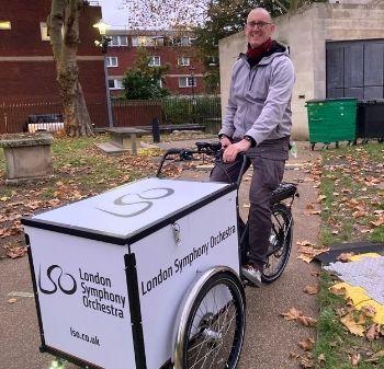 White bald man sits on a white three wheeled cargo bike