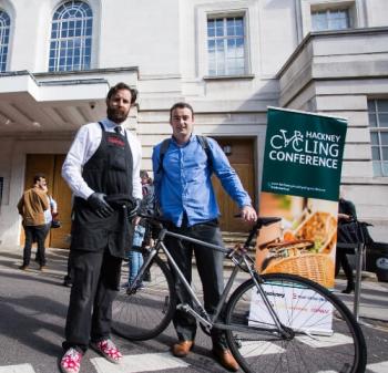 man with a bike stands next to a man without a bike looking happy 