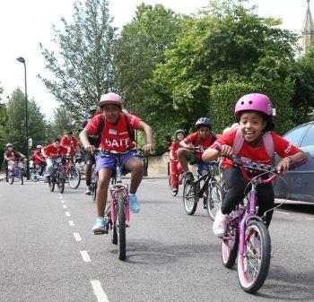 a large group of children cycle down a road 