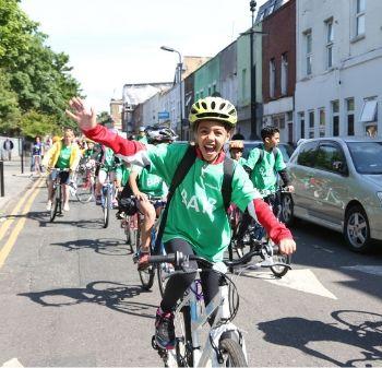 A child smiles and waves while cycling down a road 