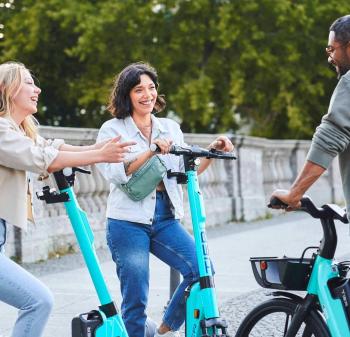  Two smiling women pose on TIER e-scooters, a smiling man poses on a TIER e-bike